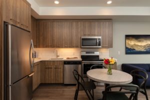 Interior view of The Shore Kelowna suites, including a state of the art kitchen with modern decor, wooden cabinets, and stainless steel appliances.