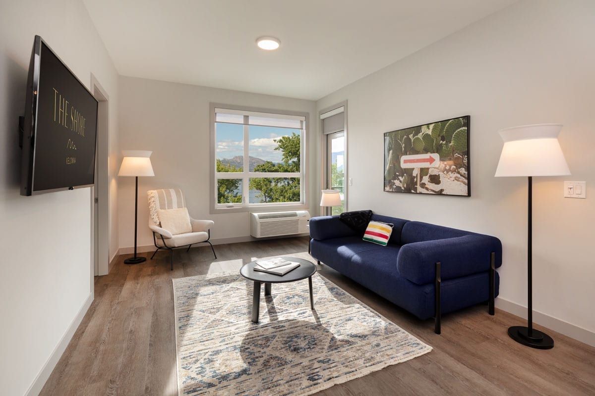 A living room in a suite at The Shore Kelowna, with a couch, chair, flatscreen tv and view over the lake