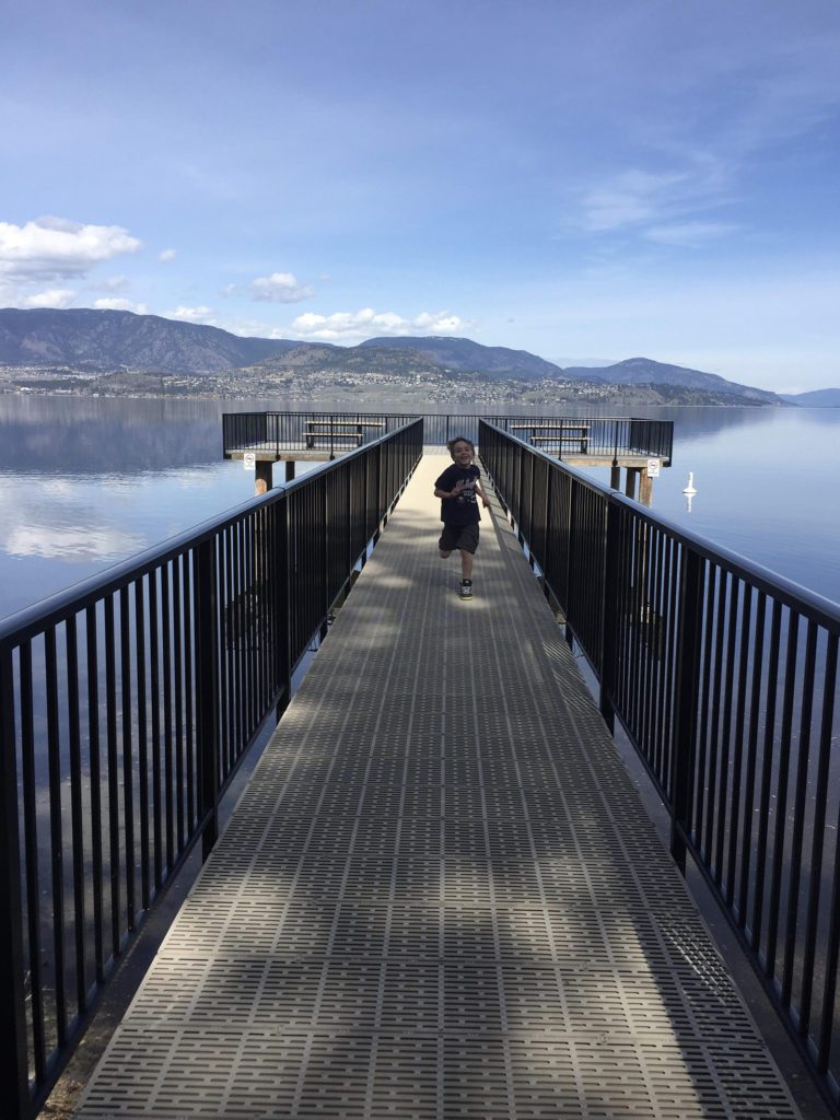 Young boy running on the dock at Bertram Creek Park, with Okanagan Lake in the background. Photo by Lyndsay Therrien.