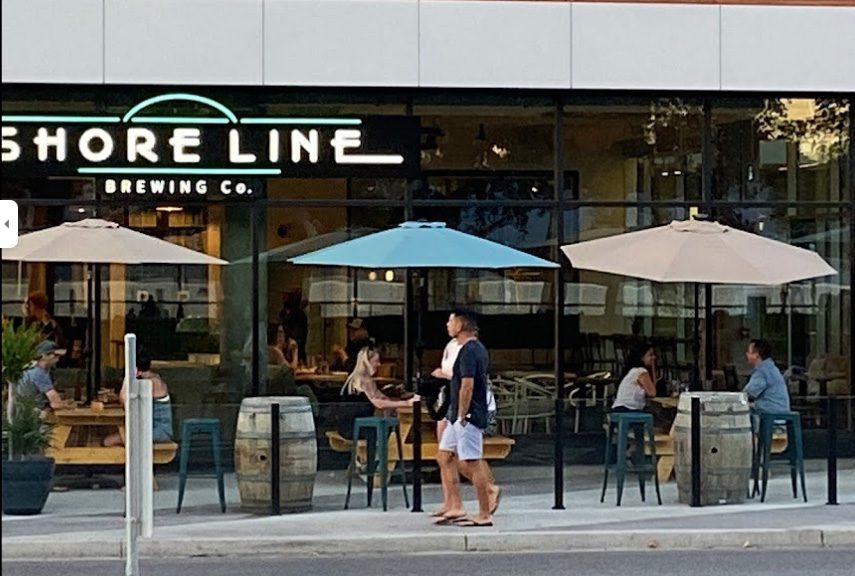 Shoreline brewing front exterior with sign and people sitting under umbrellas on their outdoor patio