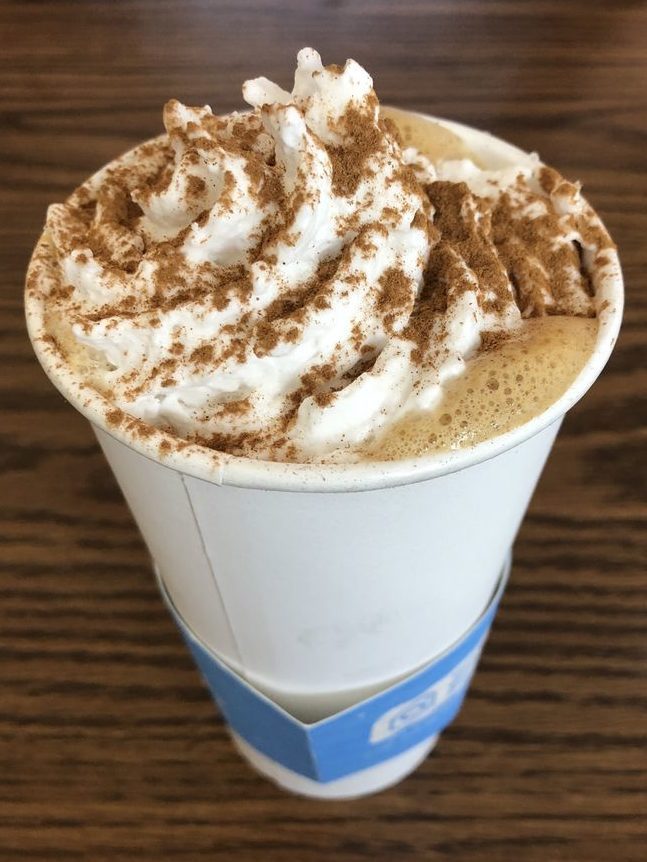 a vegan latte at naked cafe in kelowna, shown in a to-go cup with coconut whipped cream on top and cinnamon sprinkled on top