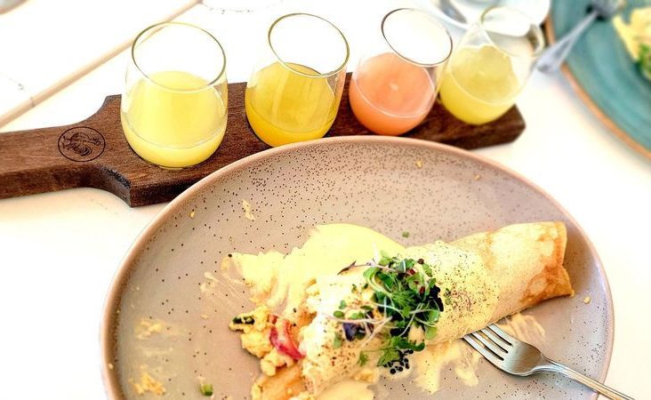 oeb kelowna breakfast on a white surface, featuring crepes and a flight of four mimosas