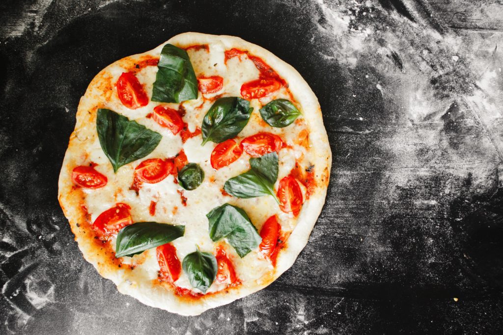 a top-down view of a classic margarita pizza with grape tomatoes, basil and mozzarella