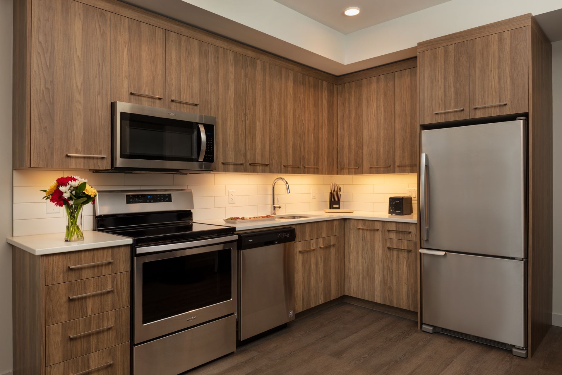 The Shore Kelowna 1 Bedroom plus Den Suite Kitchen with wood cabinets and stainless steel appliances, a vase of flowers on the countertop