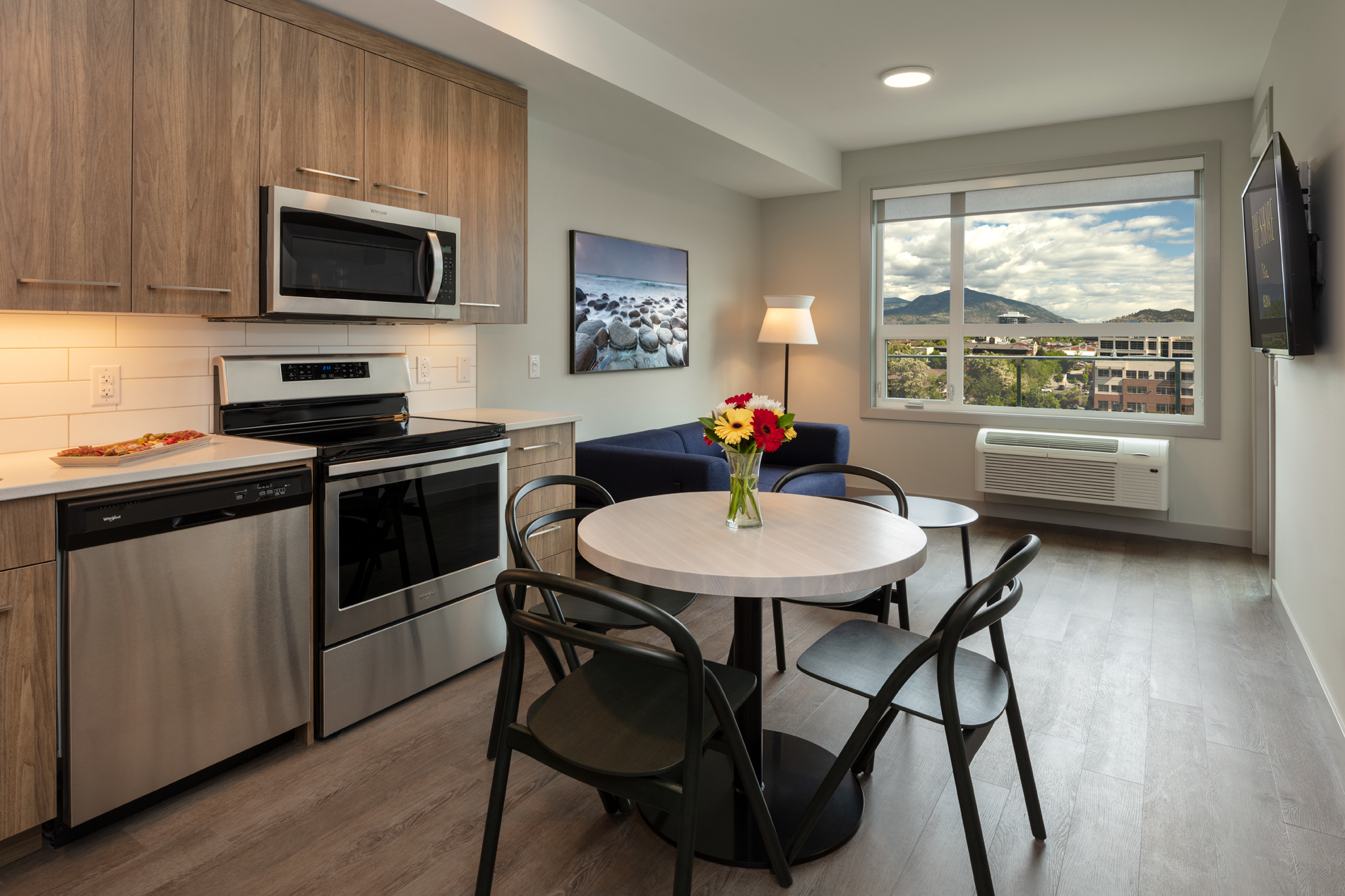 the kitchen of the 1 bedroom plus den suite at The Shore Kelowna, with a view of mountains out the window and stainless steel appliances