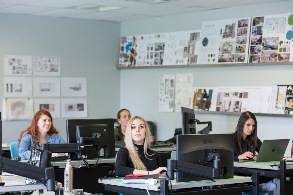four students sitting at desks with computer monitors in a classroom decorated with interior design photos and diagrams, highlighting CATO college interior design program