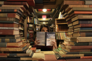 piles of books creating a window in a bookstore with a woman reading in the centre